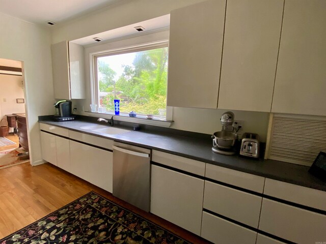 kitchen with sink, white cabinets, light hardwood / wood-style flooring, and stainless steel dishwasher