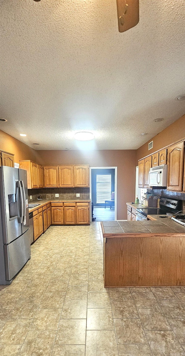 kitchen with kitchen peninsula, appliances with stainless steel finishes, a textured ceiling, and light tile floors