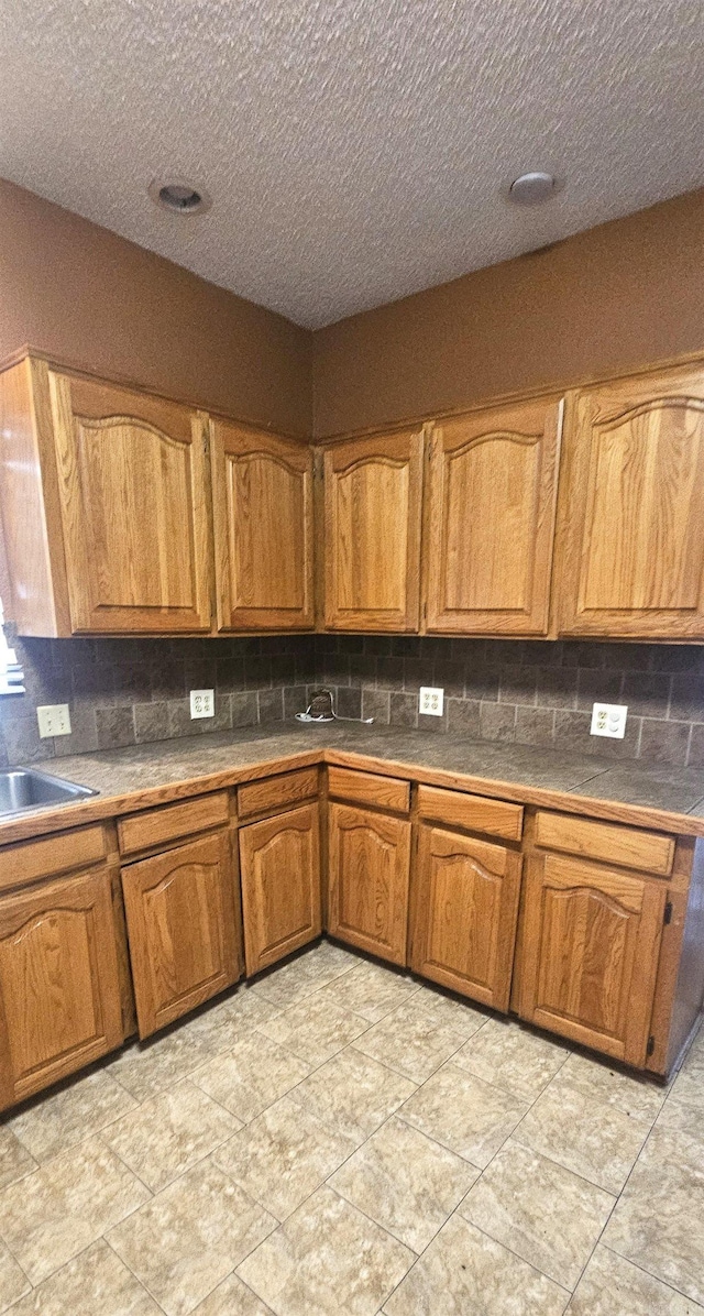 kitchen with backsplash, sink, a textured ceiling, and light tile flooring