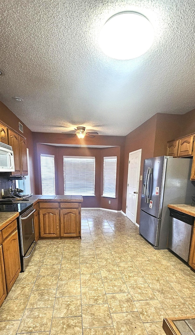 kitchen featuring appliances with stainless steel finishes, a textured ceiling, tasteful backsplash, and light tile floors