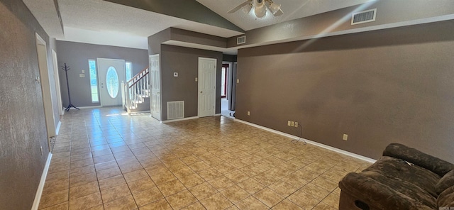 tiled empty room featuring lofted ceiling, ceiling fan, and a textured ceiling