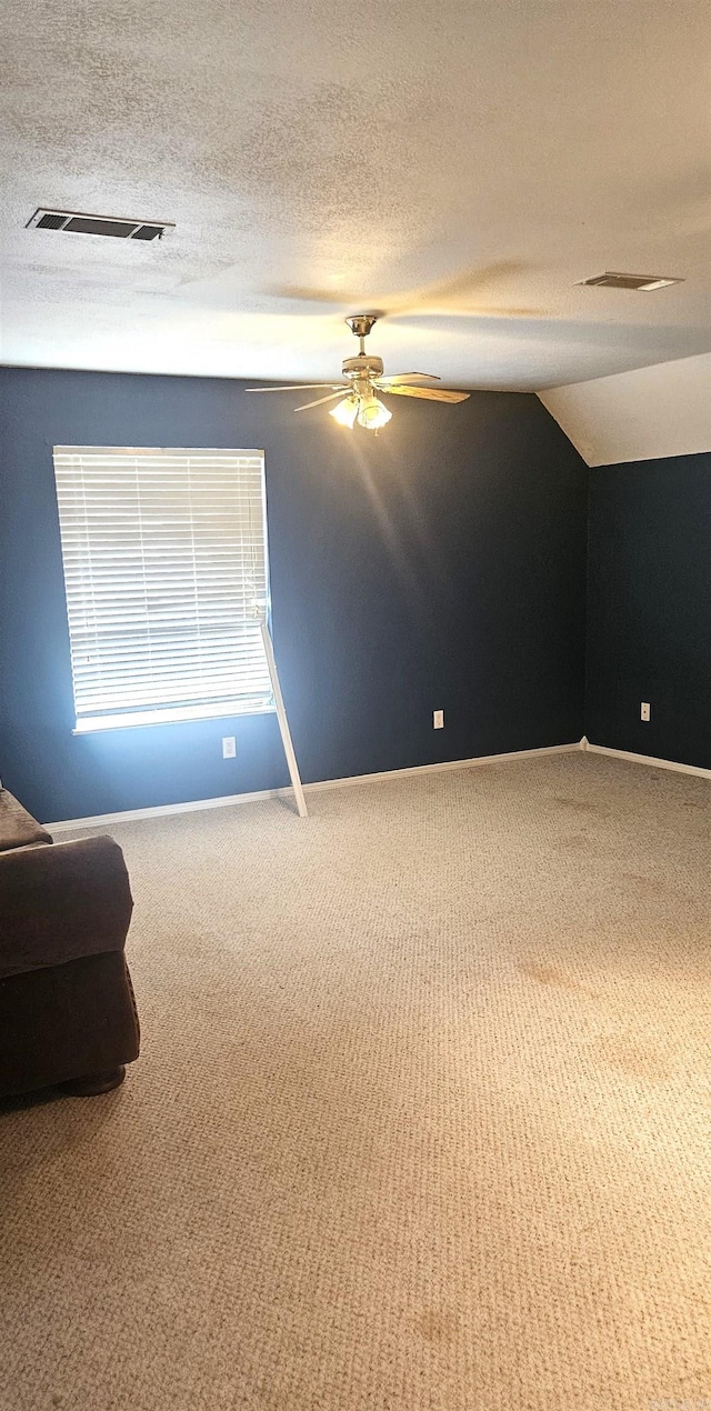 empty room featuring vaulted ceiling, carpet floors, ceiling fan, and a textured ceiling