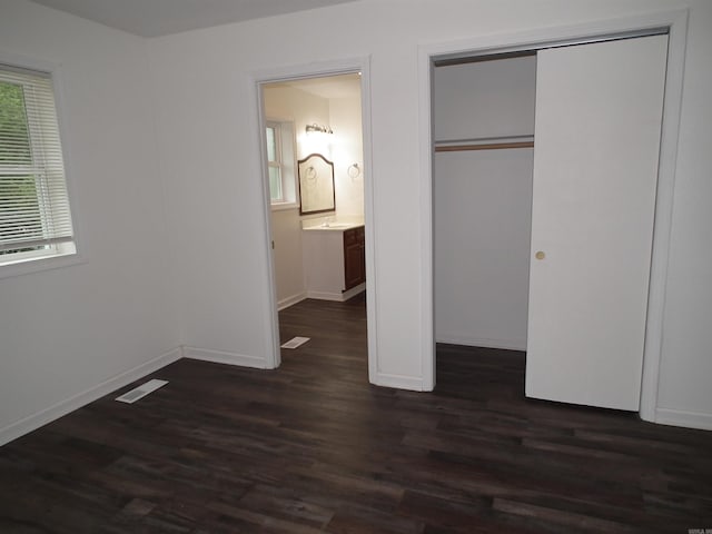 unfurnished bedroom with a closet, dark wood-type flooring, ensuite bathroom, and multiple windows