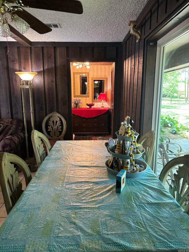 dining room featuring a textured ceiling, ceiling fan, and wooden walls