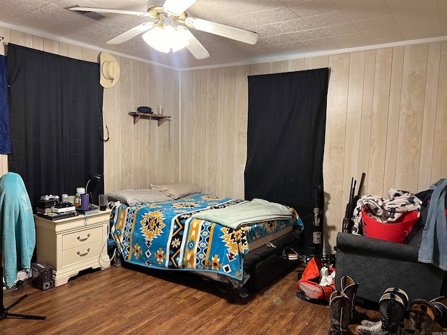 bedroom with ornamental molding, wood-type flooring, ceiling fan, and wooden walls