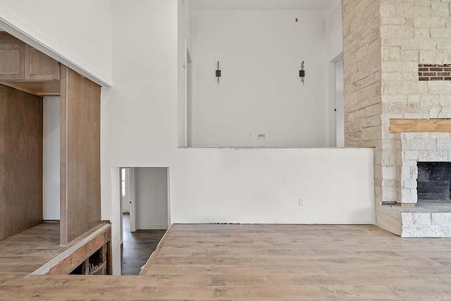 unfurnished living room with hardwood / wood-style flooring, a stone fireplace, and a towering ceiling