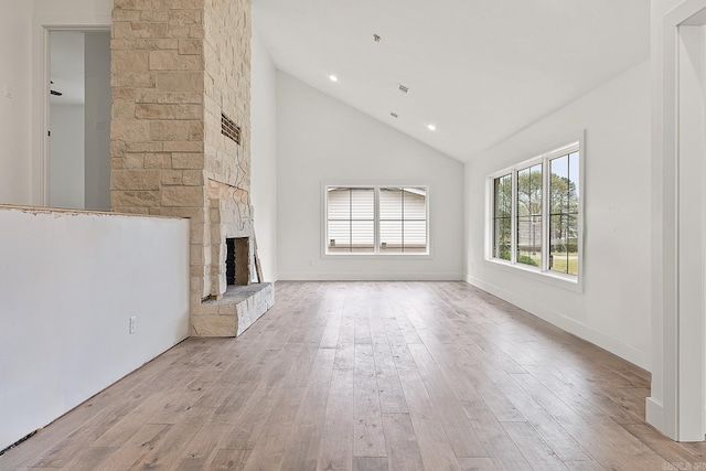 unfurnished living room featuring high vaulted ceiling, a fireplace, and light wood-type flooring