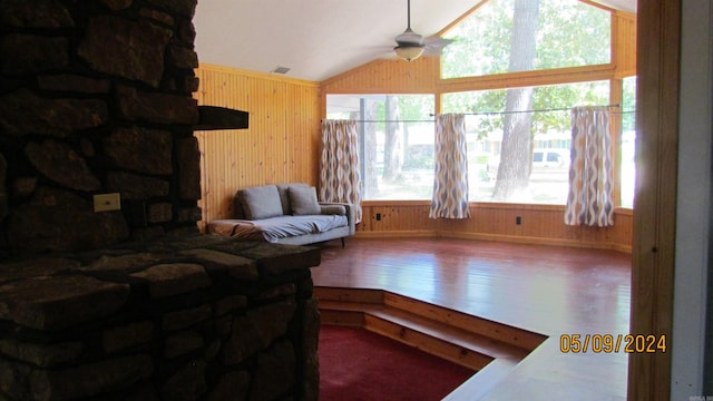 living room featuring ceiling fan, vaulted ceiling, hardwood / wood-style flooring, and wooden walls