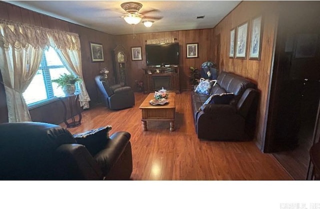 living room with hardwood / wood-style floors, ceiling fan, and wood walls