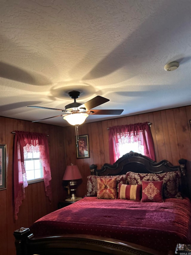 bedroom with ceiling fan, a textured ceiling, and wood walls