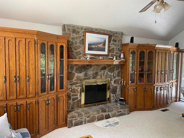 carpeted living room with vaulted ceiling, ceiling fan, a stone fireplace, and a textured ceiling