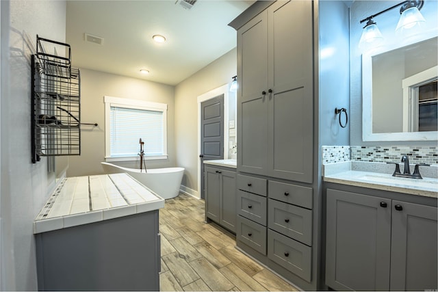 bathroom with vanity, a bath to relax in, backsplash, and wood-type flooring