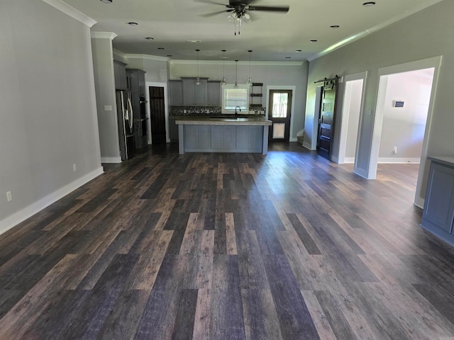 kitchen featuring dark wood-type flooring, a kitchen island with sink, stainless steel fridge, and pendant lighting