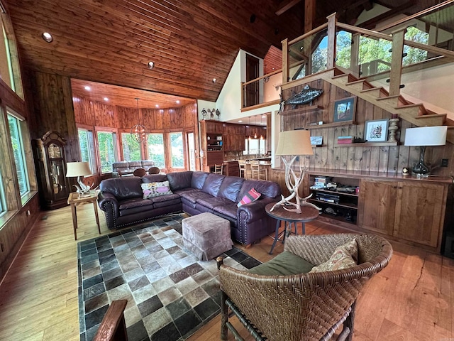 living room featuring high vaulted ceiling, wood-type flooring, wooden walls, and an inviting chandelier