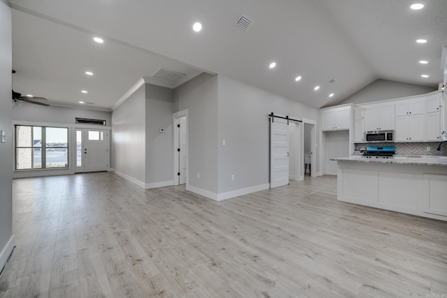 kitchen featuring tasteful backsplash, white cabinetry, range, light stone counters, and a barn door