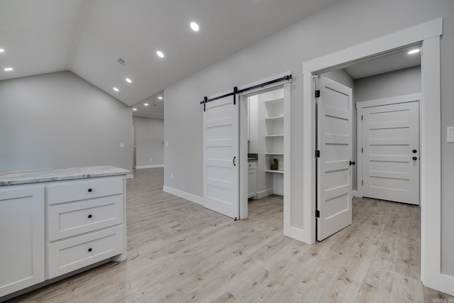 interior space featuring vaulted ceiling, a barn door, and light hardwood / wood-style floors