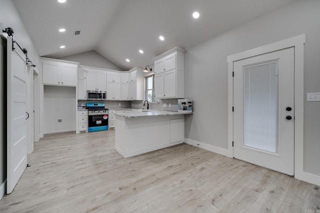 kitchen featuring white cabinetry, light stone counters, kitchen peninsula, stainless steel appliances, and a barn door