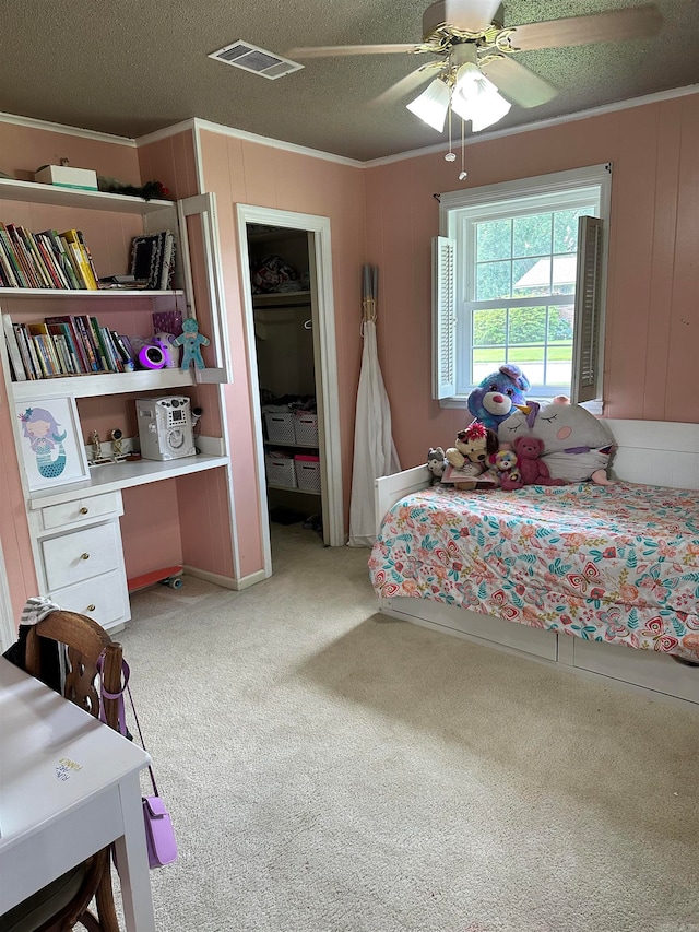 carpeted bedroom featuring ceiling fan, a closet, crown molding, a spacious closet, and a textured ceiling