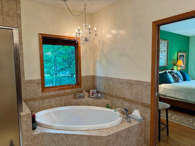 bathroom featuring a notable chandelier, hardwood / wood-style flooring, and tiled tub