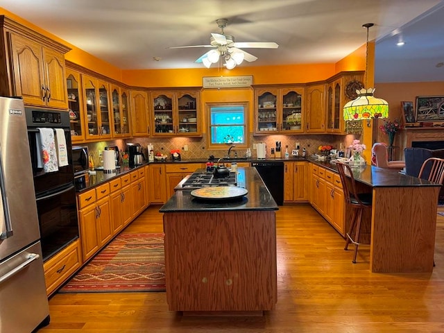 kitchen featuring ceiling fan, light hardwood / wood-style flooring, black appliances, backsplash, and a center island