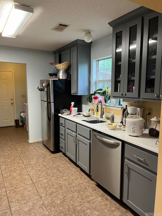 kitchen with sink, a textured ceiling, light tile patterned floors, stainless steel dishwasher, and gray cabinetry