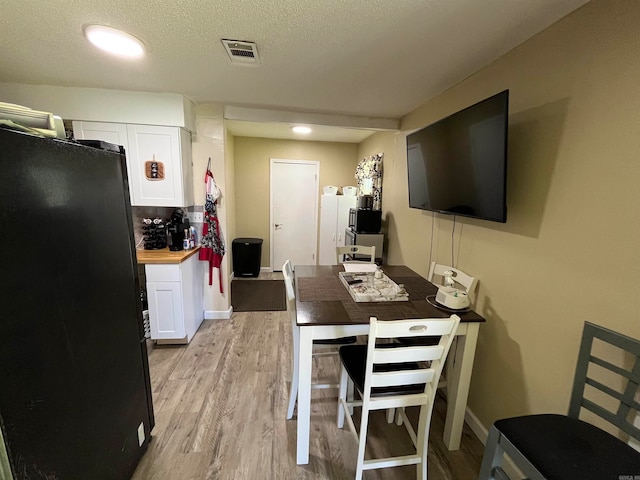 kitchen featuring black fridge, light hardwood / wood-style floors, butcher block counters, a textured ceiling, and white cabinets