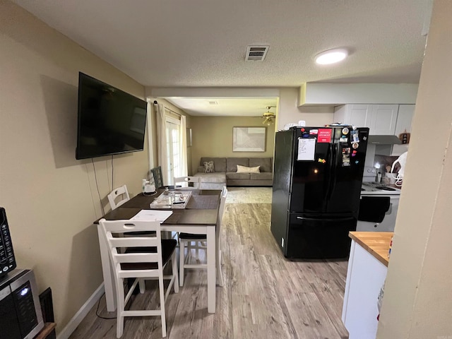 kitchen with light hardwood / wood-style flooring, wooden counters, black refrigerator, a textured ceiling, and white cabinets