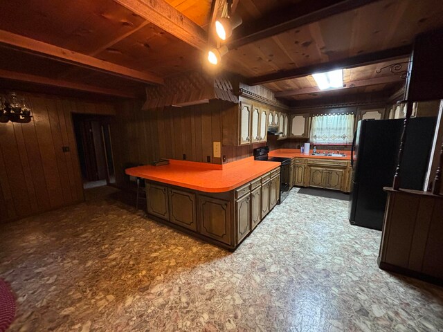 kitchen featuring dark brown cabinetry, black refrigerator, sink, wooden walls, and electric stove