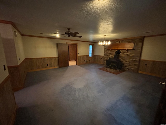 carpeted living room with brick wall, a wood stove, ceiling fan with notable chandelier, ornamental molding, and a textured ceiling