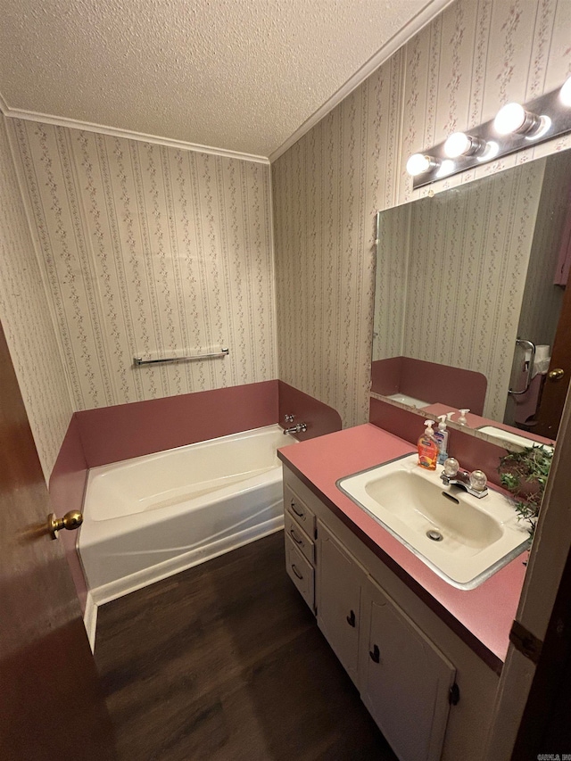 bathroom featuring a bath to relax in, a textured ceiling, ornamental molding, hardwood / wood-style flooring, and large vanity