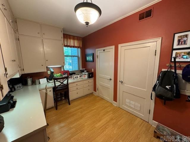 kitchen with hanging light fixtures, white cabinetry, light wood-type flooring, and crown molding