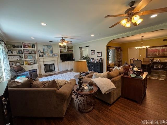 living room with ornamental molding, built in shelves, wood-type flooring, and ceiling fan with notable chandelier