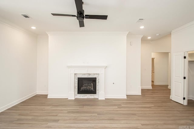 unfurnished living room featuring ceiling fan, a stone fireplace, light hardwood / wood-style flooring, and crown molding