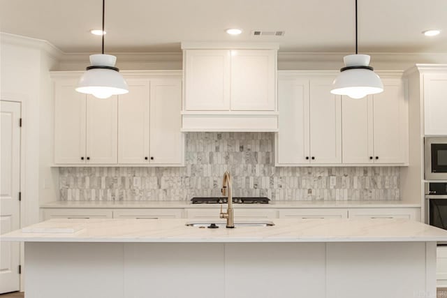 kitchen with light stone counters, hanging light fixtures, an island with sink, and tasteful backsplash