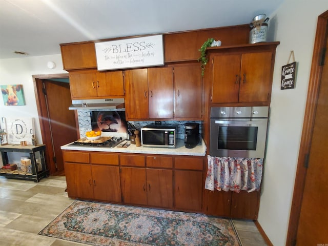 508 State St, Greenway, AR 72430 - kitchen featuring appliances with stainless steel finishes, brown cabinets, light countertops, under cabinet range hood, and tasteful backsplash