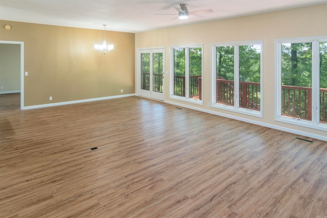 spare room featuring a healthy amount of sunlight, hardwood / wood-style flooring, and ceiling fan with notable chandelier