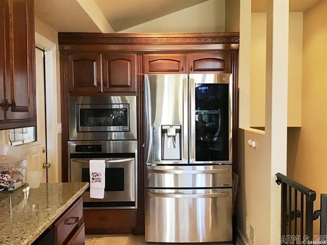 kitchen with light stone counters, stainless steel appliances, and vaulted ceiling