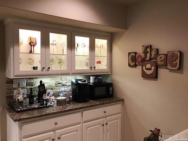 bar with backsplash, dark stone countertops, and white cabinetry