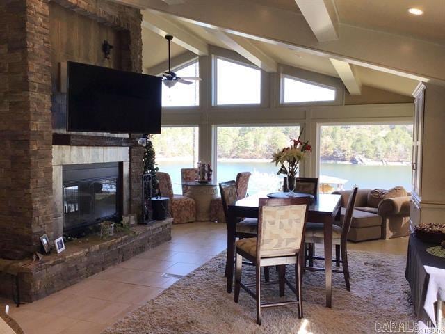 tiled dining area with vaulted ceiling with beams, ceiling fan, a stone fireplace, and a wealth of natural light