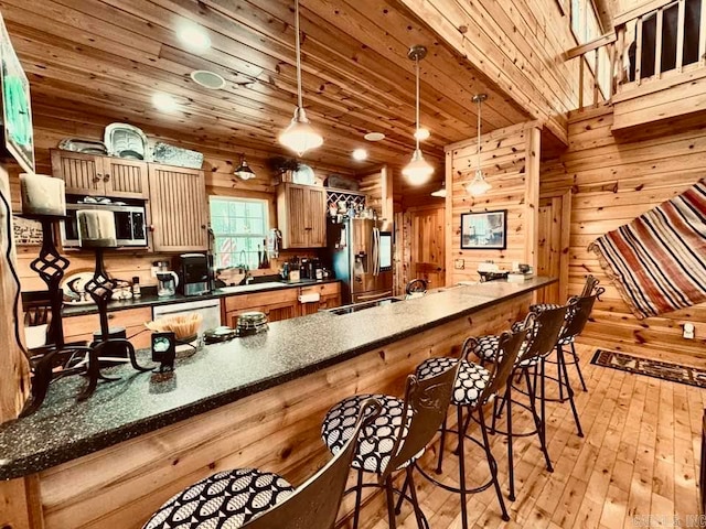 kitchen featuring hanging light fixtures, light wood-type flooring, appliances with stainless steel finishes, wooden walls, and sink