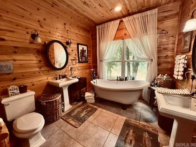 bathroom featuring tile flooring, a bath to relax in, wood ceiling, wood walls, and toilet