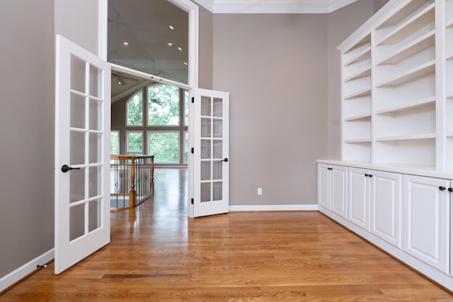 empty room with built in shelves, light wood-type flooring, french doors, and crown molding