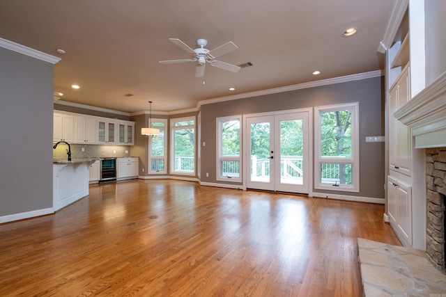 unfurnished living room with light hardwood / wood-style flooring, beverage cooler, ceiling fan, ornamental molding, and sink