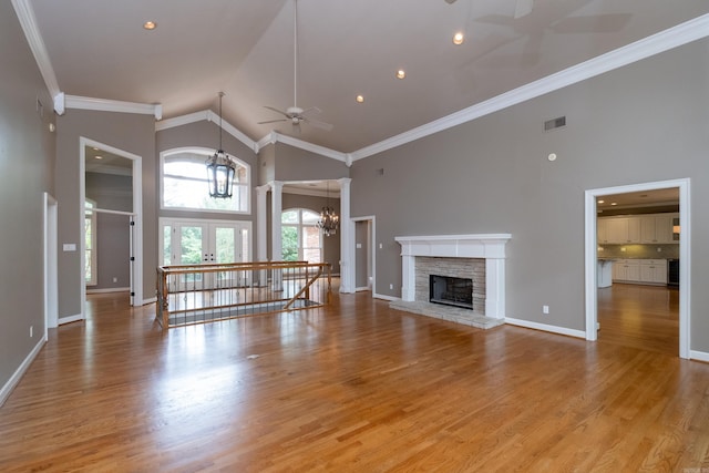 unfurnished living room featuring a fireplace, ceiling fan with notable chandelier, crown molding, light wood-type flooring, and high vaulted ceiling