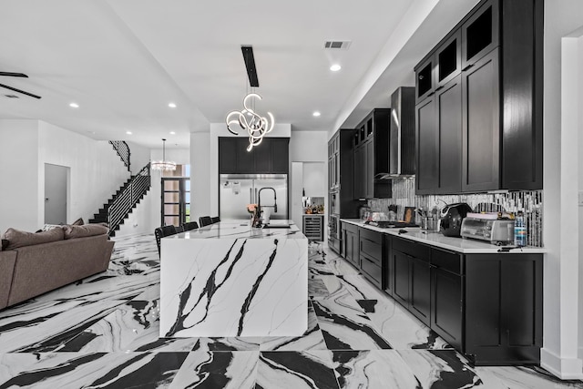 kitchen with decorative backsplash, wall chimney exhaust hood, stainless steel appliances, a spacious island, and hanging light fixtures