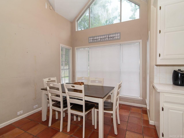 dining area featuring dark tile patterned floors and high vaulted ceiling