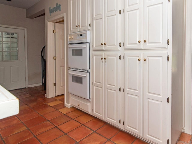 kitchen featuring double oven, white cabinets, and light tile patterned flooring