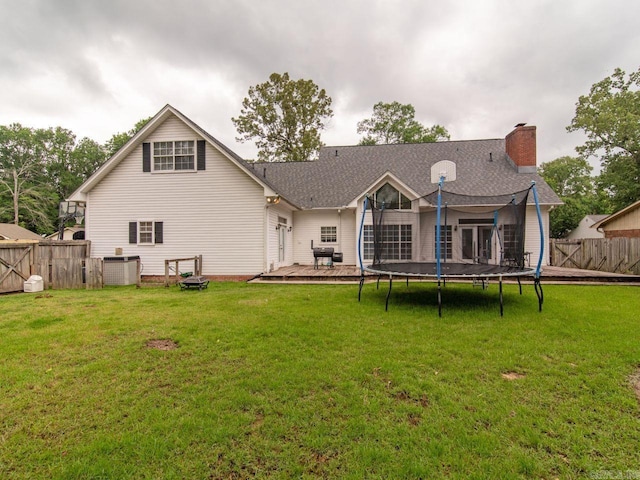 rear view of property with a trampoline, a yard, and central AC