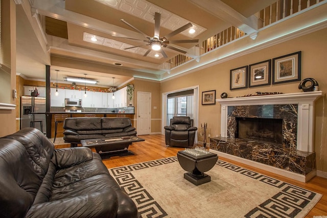 living room with ceiling fan, light wood-type flooring, ornamental molding, and a high ceiling