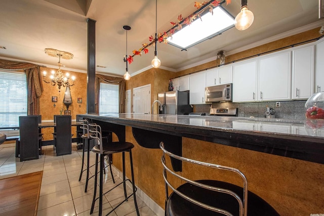 kitchen with stainless steel appliances, decorative light fixtures, dark stone countertops, white cabinetry, and light tile patterned flooring